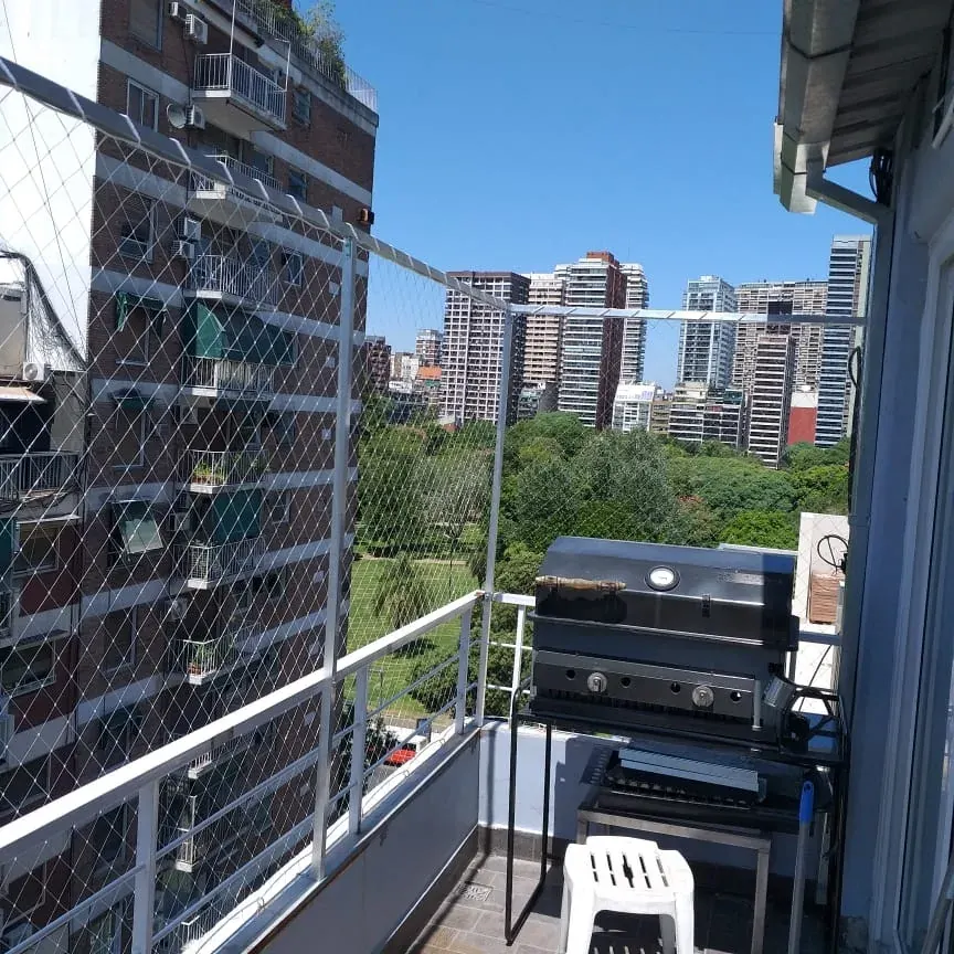 Balcón en altura cerrado con red frente a torres y árboles.