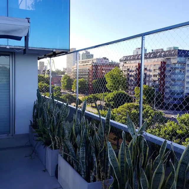 Balcón con plantas y red sobre la baranda de vidrio.