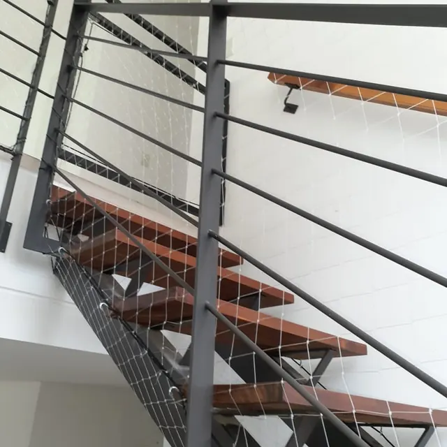 Escalera de peldaños de madera con baranda metálica y red transparente.