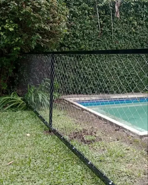Cerco de pileta con red y postes negros en un jardín.