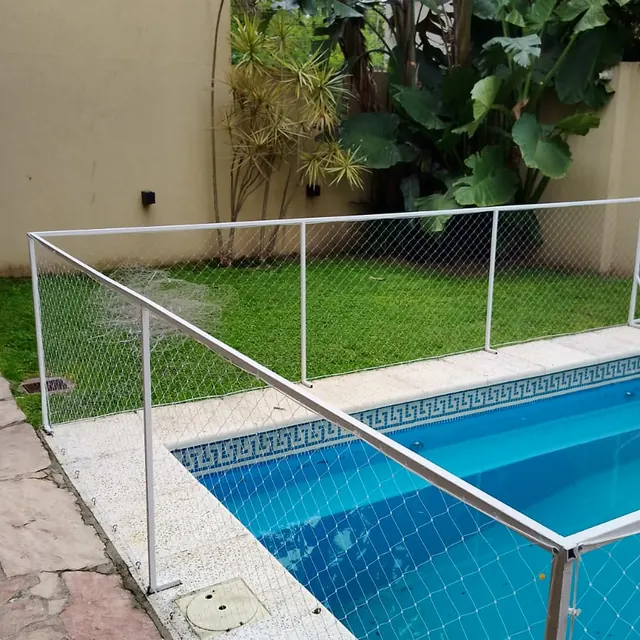 Cerco de pileta con caños blancos y red en un patio con jardín.